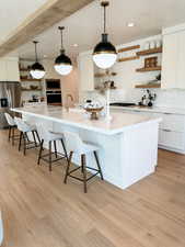 Kitchen featuring stainless steel fridge, a large island with sink, light hardwood / wood-style floors, and white cabinets