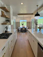 Kitchen with white cabinetry, black gas cooktop, light hardwood / wood-style floors, decorative light fixtures, and stainless steel dishwasher