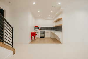 Sink, backsplash, wine cooler, white cabinets, and light wood-type flooring