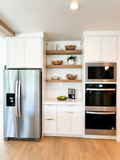 Kitchen featuring built in microwave, tasteful backsplash, stainless steel fridge with ice dispenser, light wood-type flooring, and white cabinets