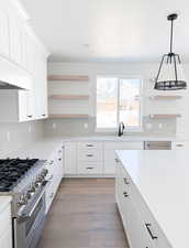 Kitchen with pendant lighting, sink, white cabinetry, high end range, and light wood-type flooring