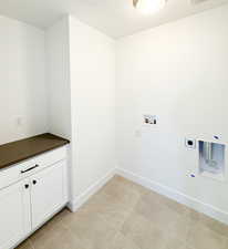 Washroom with cabinets, light tile patterned floors, hookup for a washing machine, hookup for an electric dryer, and a textured ceiling