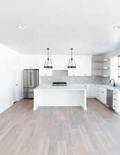 Kitchen featuring sink, white cabinetry, hanging light fixtures, stainless steel appliances, and a center island