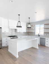 Kitchen featuring decorative light fixtures, appliances with stainless steel finishes, white cabinets, and a kitchen island