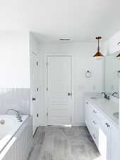 Bathroom with tiled tub, vanity, and tile patterned flooring