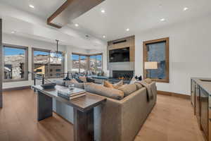 Living room with light hardwood / wood-style flooring, a notable chandelier, beam ceiling, and a fireplace