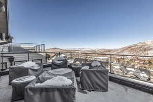 Snow covered patio with a balcony, grilling area, and a mountain view