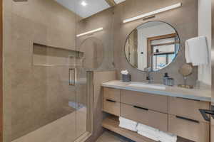 Bathroom with vanity, an enclosed shower, and tile walls