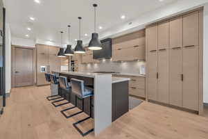 Kitchen with pendant lighting, a breakfast bar, a kitchen island with sink, stainless steel gas cooktop, and light wood-type flooring