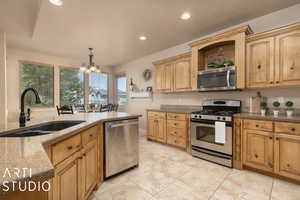 Kitchen featuring sink, appliances with stainless steel finishes, hanging light fixtures, a notable chandelier, and light stone countertops