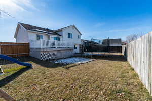 Back of house featuring a trampoline, a wooden deck, a yard, and a playground