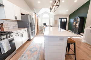 Kitchen featuring lofted ceiling, appliances with stainless steel finishes, white cabinetry, a kitchen island, and a barn door