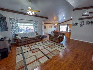 Living room featuring ceiling fan, hardwood / wood-style floors, vaulted ceiling, and a textured ceiling