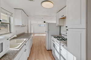 Kitchen with sink, white appliances, a healthy amount of sunlight, light hardwood / wood-style floors, and white cabinets