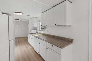 Kitchen with white cabinetry, sink, white appliances, and light wood-type flooring