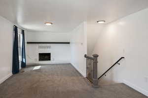 Unfurnished living room featuring a brick fireplace and carpet flooring