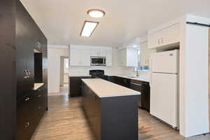 Kitchen with appliances with stainless steel finishes, sink, white cabinets, a center island, and light hardwood flooring