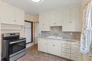 Kitchen with white refrigerator, sink, white cabinets, and stainless steel range with electric cooktop