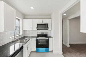 Kitchen with sink, dark stone countertops, stainless steel appliances, white cabinets, and light carpet