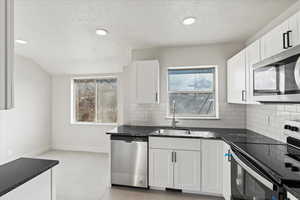 Kitchen featuring appliances with stainless steel finishes, sink, dark stone countertops, and white cabinets