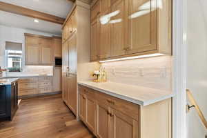 Kitchen with built in microwave, beam ceiling, light stone countertops, light hardwood / wood-style floors, and light brown cabinetry, built in cabinet fridge