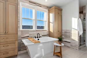 Primary Bathroom with tile patterned floors, tile walls, and a free standing tub