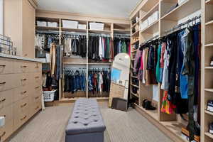 Spacious walk in closet featuring light carpet with build in dresser and vanity, 1 of 2 primary bedroom closets