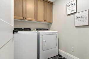 Clothes washing area featuring cabinets, washer and clothes dryer, and dark tile patterned flooring