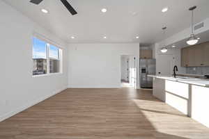 Kitchen with decorative light fixtures, sink, backsplash, stainless steel fridge with ice dispenser, and light wood-type flooring