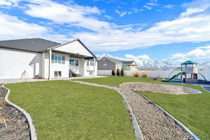 Rear view of house featuring a playground, a mountain view, and a yard