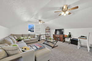 Living room with ceiling fan, vaulted ceiling, a textured ceiling, and carpet