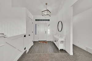 Foyer entrance with dark colored carpet and an inviting chandelier