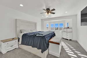 Bedroom with a textured ceiling, light colored carpet, and ceiling fan