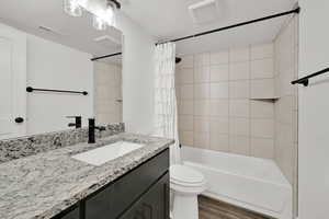 Full bathroom with shower / tub combo with curtain, hardwood / wood-style flooring, vanity, a textured ceiling, and toilet