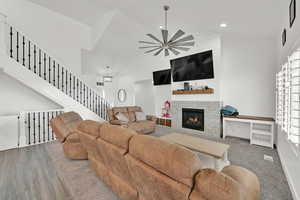 Living room with ceiling fan, wood-type flooring, a fireplace, and high vaulted ceiling