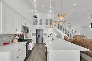 Kitchen with black range with gas cooktop, tasteful backsplash, decorative light fixtures, a center island with sink, and stainless steel fridge