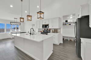 Kitchen with a kitchen island with sink, hanging light fixtures, white cabinets, and appliances with stainless steel finishes