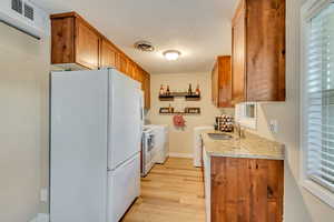 Kitchen featuring a wealth of natural light, sink, white refrigerator, independent washer and dryer, and light hardwood / wood-style floors