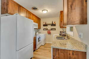 Kitchen with sink, light stone counters, light hardwood / wood-style floors, washing machine and dryer, and white appliances