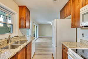 Kitchen with sink, white appliances, light hardwood / wood-style flooring, light stone countertops, and a textured ceiling