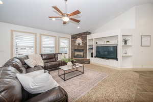 Living room with ceiling fan, lofted ceiling, a fireplace, and built in shelves