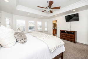 Bedroom with a raised ceiling, multiple windows, ceiling fan, and ensuite bath