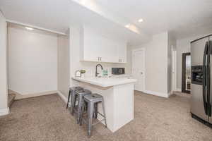 Kitchen with stainless steel refrigerator with ice dispenser, white cabinetry, a kitchen bar, and light colored carpet