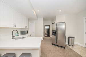 Kitchen featuring stainless steel fridge with ice dispenser, sink, white cabinets, a kitchen breakfast bar, and kitchen peninsula