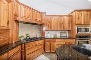 Kitchen with decorative backsplash, stainless steel appliances, and dark stone counters