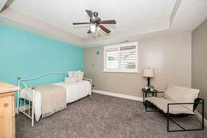 Bedroom with dark carpet, a textured ceiling, ceiling fan, and a tray ceiling