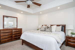 Bedroom featuring a raised ceiling, crown molding, light carpet, and ceiling fan