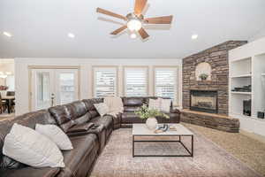 Carpeted living room featuring vaulted ceiling, a stone fireplace, ceiling fan, and french doors