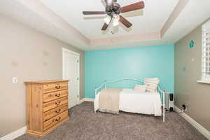 Bedroom featuring a tray ceiling, dark carpet, a textured ceiling, and ceiling fan