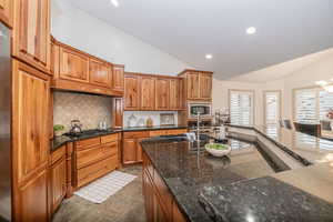 Kitchen featuring lofted ceiling, sink, dark stone counters, stainless steel appliances, and backsplash